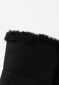 Botín negro con un exterior de cuero sintético texturizado y un puño de forro polar negro y suave en la parte superior, con un detalle de costura lisa.