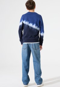 Sudadera de color azul marino con patrón de teñido anudado en blanco; material de algodón suave, cuello redondo, puños acanalados, combinada con jeans de corte relajado.