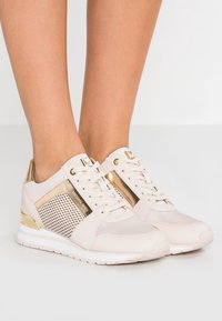Beige athletic sneakers with suede and mesh panels, gold accents, lace-up closure, and a cushioned sole for comfort.
