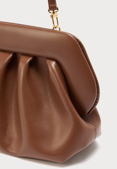 Καφέ δερμάτινη τσάντα χειρός με συγκεντρωμένες λεπτομέρειες και κούμπωμα και σύνδεσμοι ιμάντα σε χρυσό τόνο, που παρουσιάζει μαλακή, λεία υφή και δομημένο πλαίσιο.