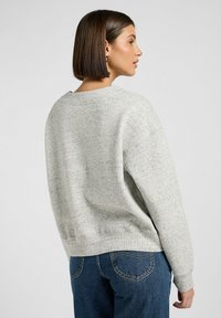 Ljusgrå sweatshirt med textilstruktur, lös passform och ribbad nederkant. Åtsidan med mörkblå jeans som har fickor och detaljerad sömnad.