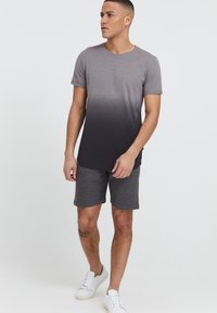 Graues Ombre-T-Shirt, das von Hellgrau zu Dunkelgrau übergeht, kombiniert mit grauen Shorts. Das Modell trägt weiße Sneakers.