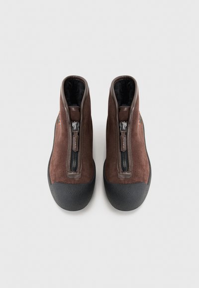 Brune ruskind ankelstøvler med en frontlynlås, en gummiforstærkning ved tåen og en blød indvendig foring. Har et lille flerfarvet emblem på siden.