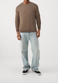 Brun stickad tröja med långa ärmar, rund halsringning, tillsammans med ljusblå denimjeans och svarta låga skor. Avslappnad passform.