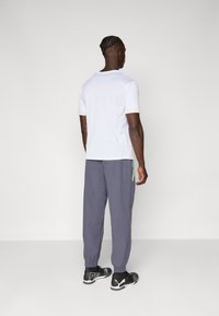 Hvid kortærmet skjorte med et struktureret stof, paired med mørkegrå joggingbukser med en grøn lynlåsdetaile og elastiske manchetter. Sorte atletiske sko.