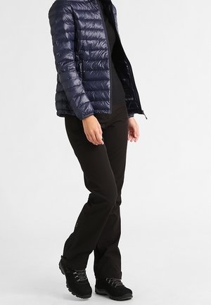 Chaqueta acolchada azul marino con costuras horizontales, camiseta negra, pantalones negros y botas de senderismo negras. Detalle de cremallera lateral en los pantalones.