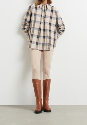 Camisa de cuadros marrón tipo botón con un ajuste relajado, leggings beige y botas marrones hasta la rodilla con suelas negras. Diseño simple con un patrón clásico.