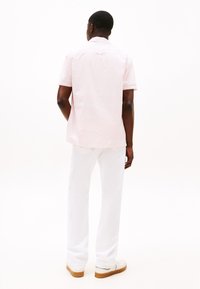 Camicia a maniche corte di colore rosa chiaro con un sottile motivo, abbinata a pantaloni bianchi e sneakers bianche, vista da dietro.