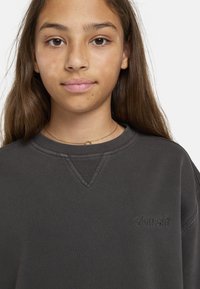 Mörkgrå sweatshirt med ribbad halsringning och broderad logotyp. Mjuk textur, avslappnad passform, med V-söm detalj vid kragen.