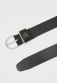 Cintura in pelle nera con fibbia in argento, dotata di un anello per fibbia marchiato. La banda è liscia con bordi puliti e una punta appuntita.