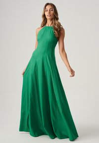 Abito verde con scollo all'americana, corpino aderente, gonna A-line fluida e texture morbida. Le cuciture dettagliate mettono in risalto la silhouette.