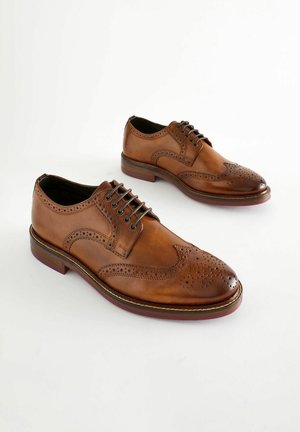 Chaussures Oxford en cuir marron avec des détails perforés, fermeture à lacets et bout arrondi. Texture lisse et semelle contrastante.