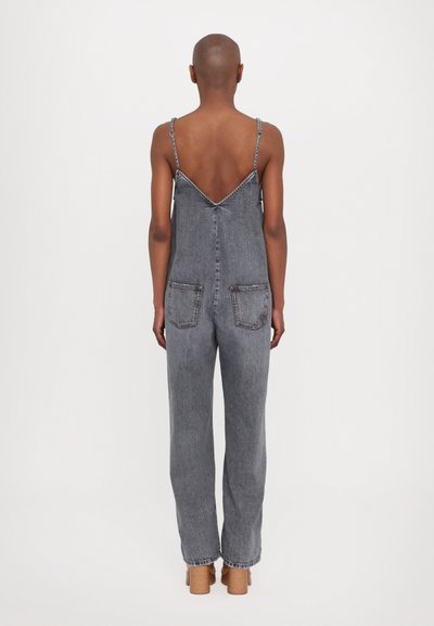 Salopette en denim avec bretelles spaghetti ajustables, couleur grise, jambes larges, dos en V et deux poches arrière avec des détails de couture visibles.