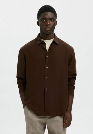 Brown button-up shirt with a collar, long sleeves, and subtle texture. Paired with light gray trousers, featuring a relaxed fit.