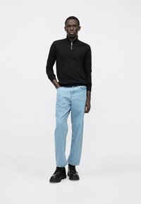 Czarny sweter z zamkiem przy szyi, jasnoniebieskie jeansy o prostych nogawkach oraz czarne sznurowane buty. Czysty design z kontrastowymi kolorami i casualowym krojem.