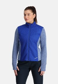 Giacca isolante blu con frontale trapuntato e maniche grigio-blu. Presenta un collo alto e chiusura con zip, realizzata in materiali morbidi.