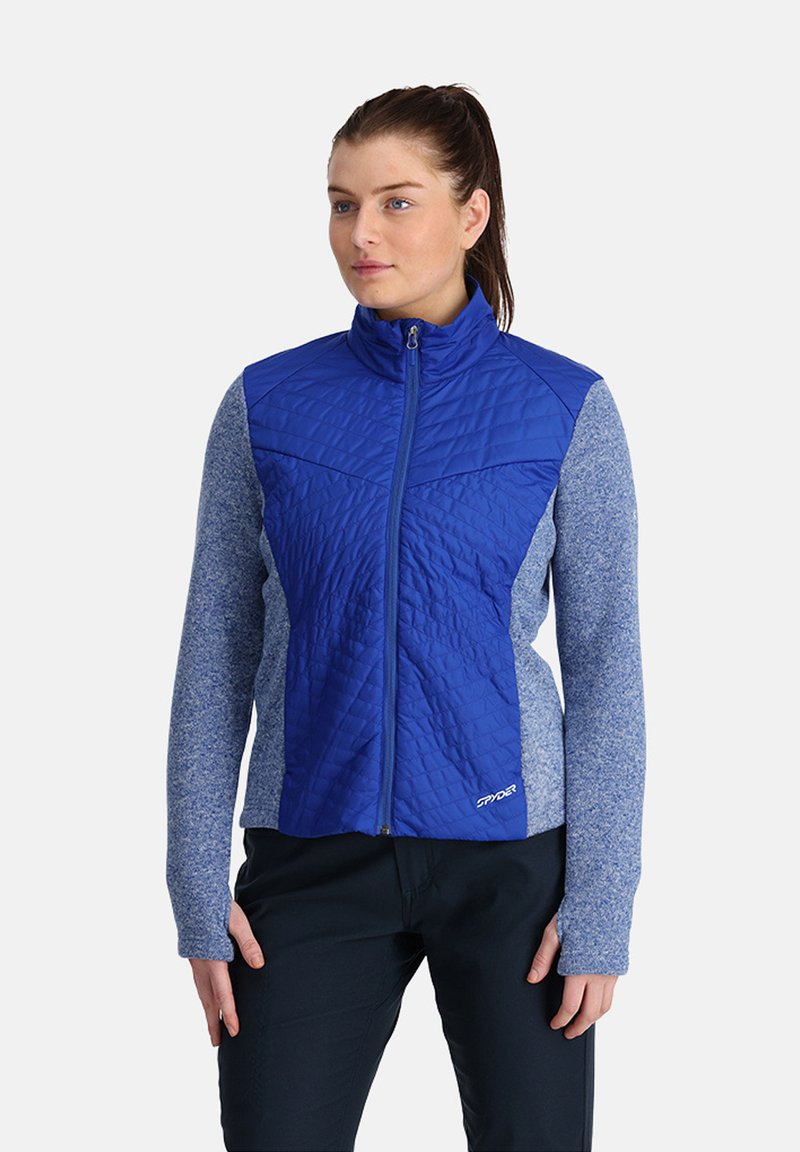 Giacca isolante blu con frontale trapuntato e maniche grigio-blu. Presenta un collo alto e chiusura con zip, realizzata in materiali morbidi.