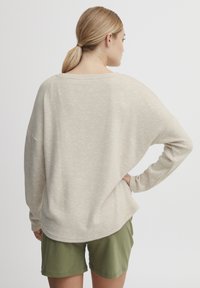 Un pull beige clair avec une coupe décontractée, un grand col, et des manches longues, associé à un short vert olive, vu de dos.