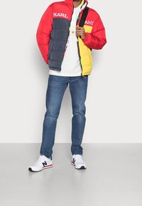 Giacca a vento colorata con sezioni rosse, grigie e gialle e dettagli con logo. Abbinata a jeans e sneakers bianche con dettagli rossi e blu navy.