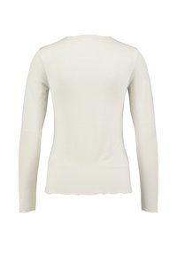 Haut à manches longues de couleur crème clair avec une coupe ajustée. Texture lisse et finitions à brut. Fabriqué en tissu doux et extensible.