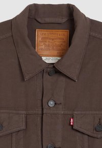 Veste Levi's marron avec col, boutons-pression noirs, poches poitrine, étiquette rouge Levi's visible, et étiquette de marque en cuir à l'intérieur du col.