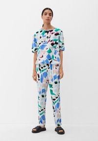 Multikleurige loungewear-set gemaakt van lichtgewicht stof; heeft abstracte patronen in blauw, groen, roze en zwart; relaxed fit; gecombineerd met sandalen.
