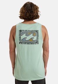 Mintgrünes ärmelloses Tanktop aus Baumwolle, mit einem bunten Wellenmotiv, das auf der Rückseite in Schwarz umrissen ist, und einer weichen Textur.