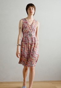 Robe sans manches avec un motif en zigzag en rose, jaune et crème, présentant un design portefeuille et une boucle en argent à la taille. Tissu léger.