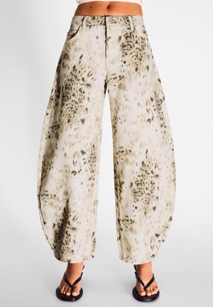 Højttaljede bukser med vid ben i beige og sort dyreprint, båret med sorte thong-sandaler på bare fødder.