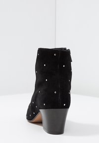 Schwarze Wildleder-Ankle Boots mit silbernen Nietenakzenten, einem gestuften Absatz, taillierter Form und einem Reißverschluss auf der Rückseite.