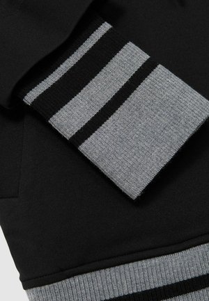 Zwarte sweatshirt met een grijze geribde manchet, voorzien van horizontale zwarte en grijze strepen. Zachte textuur met een ontspannen pasvorm ontwerp.
