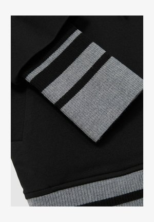 Čierna mikina s šedým rebrovaným manžetom, s horizontálnymi čiernymi a šedými pruhmi. Mäkká textúra s uvoľneným strihom.