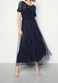 Marinblå klänning med spetstop och korta ärmar, flödande tylskirt. Kompletterad med sandaler med klara remmar.