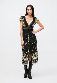 Zwarte bloemenjurk met korte pofmouwtjes, kanten randje en V-hals. Voorzien van een voorste split en een gedetailleerd zoomontwerp.