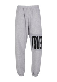 Sivé teplákové nohavice s elastickým pásom, zužujúcimi sa nohavicami a veľkým čiernym grafickým nápisom "TRUER" na boku. Mäkký materiál z bavlnenej zmesi.