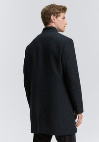Palton din amestec de lână de culoare gri închis, cu un finisaj texturat, formă ajustată, mâneci lungi și un guler clasic. Prezintă o cusătură în spate la centru.