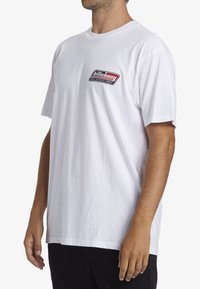 Bílá bavlněná trička, krátké rukávy, kulatý výstřih. Obsahuje malé černé a červené logo Billabong na levé části hrudi. Normální střih.