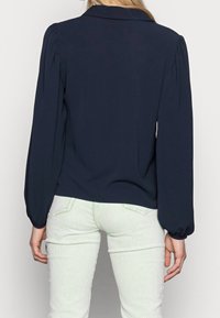 Navy blouse with long puffed sleeves, a folded collar, and a smooth texture, paired with light green corduroy pants in a straight fit.