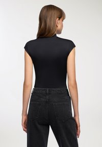 Czarny bezrękawnik z wysokim kołnierzem. Połączony z czarnymi dżinsami z wysokim stanem, które mają dwie tylne kieszenie i swobodny krój.