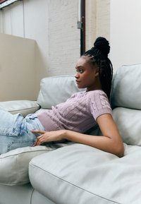 Ljusrosa kabelstickad kortärmad tröja kombinerad med ljusblå denimjeans, sittande på en vit lädersoffa med mjuk textur.