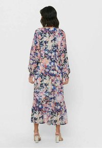 Flowy long dress in sheer fabric with a multicolored floral pattern featuring shades of blue, pink, and cream, finished with a ruffled hem.