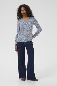 Hellblaue langärmelige Bluse mit V-Ausschnitt und weißem Blumenmuster, kombiniert mit dunkelblauen weit geschnittenen Jeans und braunen Wildlederschuhen.