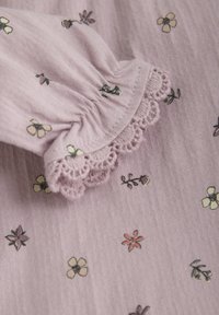 Tissu violet clair avec une finition texturée ; présente des fleurs brodées de différentes couleurs ; détails de manches élastiques avec dentelle.