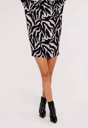 Woman wearing a black and white zebra print mini dress paired with black pointed-toe ankle boots, standing with crossed legs.