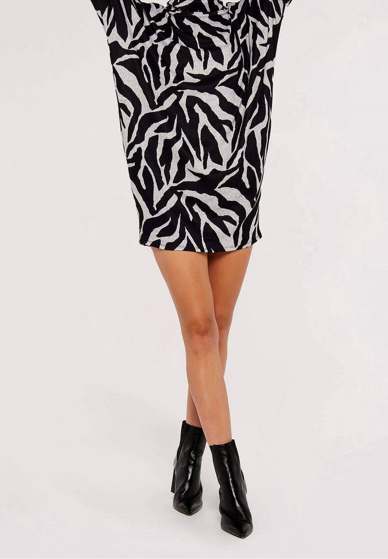 Femme portant une mini-robe imprimé zèbre noir et blanc associée à des bottines noires à bout pointu, debout les jambes croisées.