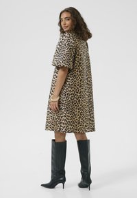 Leopardimustriga kleit lühikeste varrukatega, voolav vorm ja põlvepikkus, kombineeritud mustade põlvekohuste kontsakingadega. Sile kangastekstuuri.