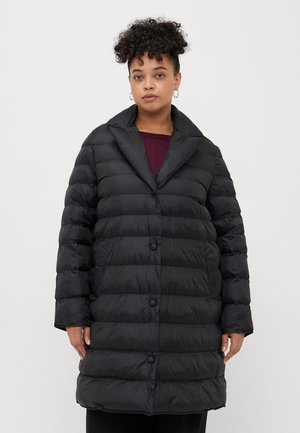 Svart pufferjakke med løs passform, som har store knapper, spitsekant og quiltet tekstur. Forlenger ermer og knelengde design.