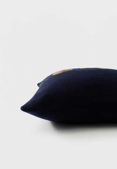 Τετράγωνο μαξιλάρι σε ναυτικό μπλε χρώμα με μερικό κεντητό σχέδιο, τοποθετημένο σε λευκή επιφάνεια.