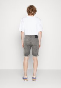 Shorts de mezclilla gris con dobladillos enrollados, con bolsillos traseros y una etiqueta de cuero negra. Combinados con una camiseta blanca y zapatillas de colores.