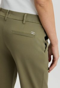 Pantaloni verde oliva con una texture liscia, dotati di una tasca posteriore con un particolare hardware decorativo in argento e tasche laterali.